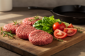 Grass-fed hamburger patties with vegetables on wooden board